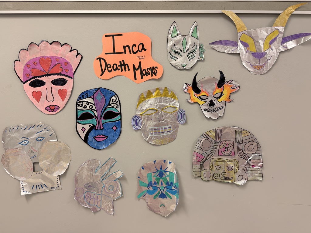 A collection of handmade masks and paper cutouts arranged on a wall. They feature various designs, including horned and animal motifs.