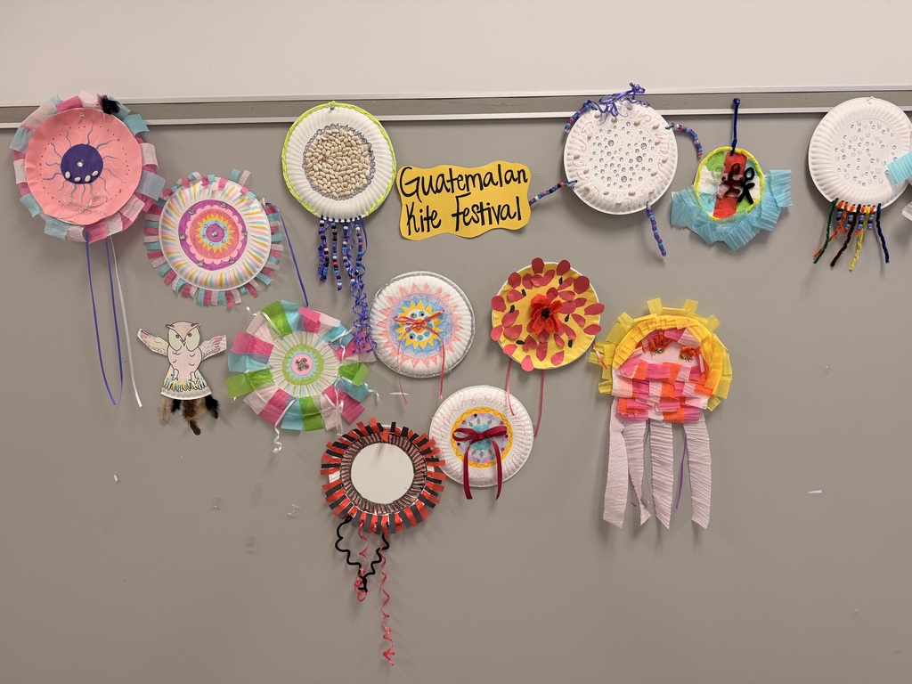 Colorful paper crafts, including circles and other shapes, hang on a gray wall with a yellow sign reading "Guests/Guests."