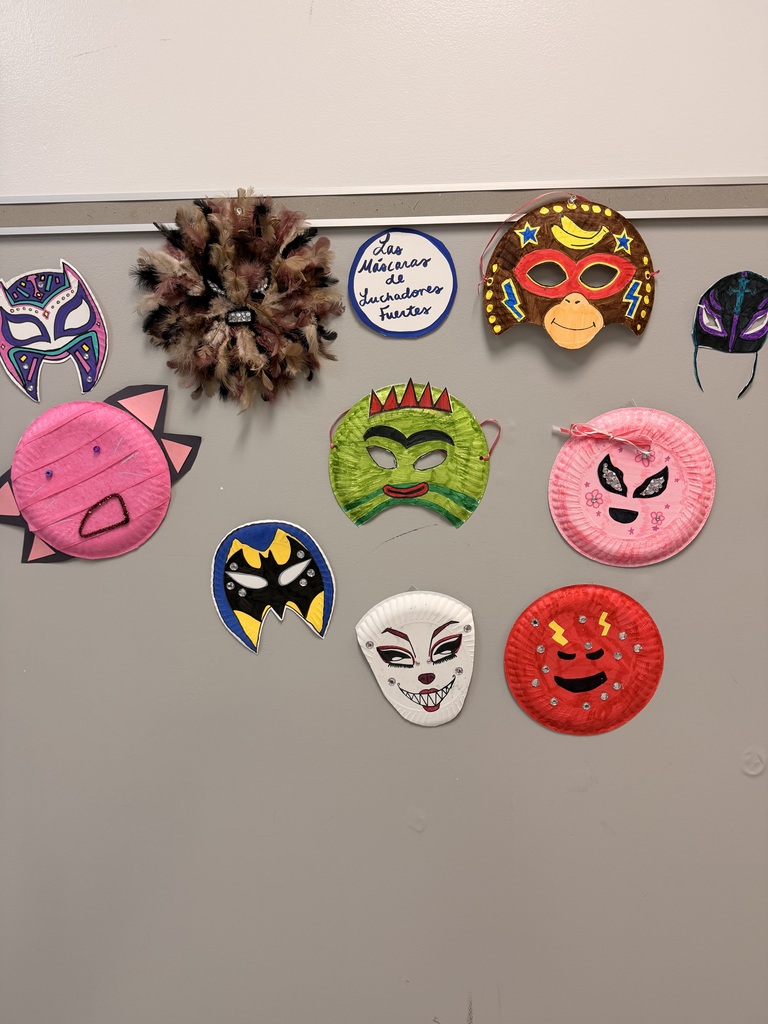 Multiple hand-crafted masks, in various colors and styles, are pinned to a white background.
