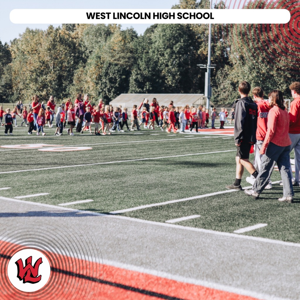 Many people in red shirts walk across a field with white lines and a large white W in the bottom left.