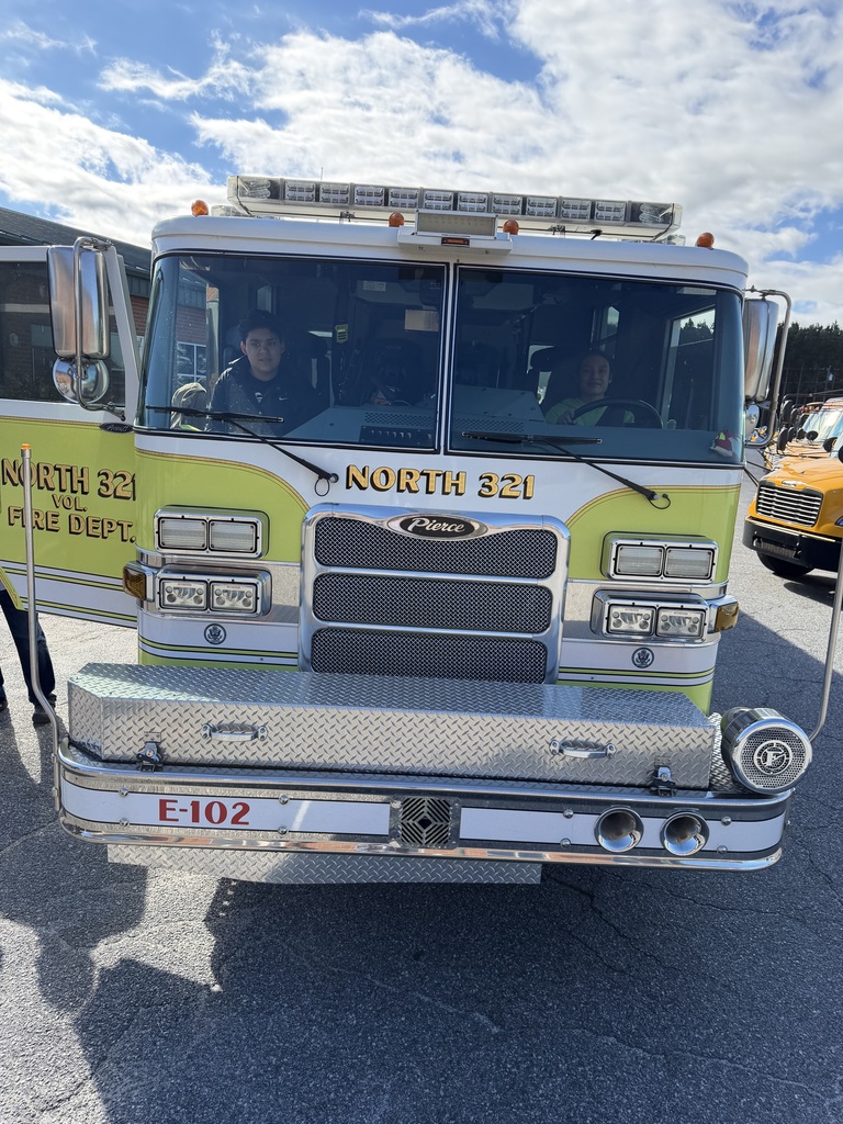 Fire truck with yellow and black paint. Number 321 on front. Two people seated inside. Bright sky in the background.