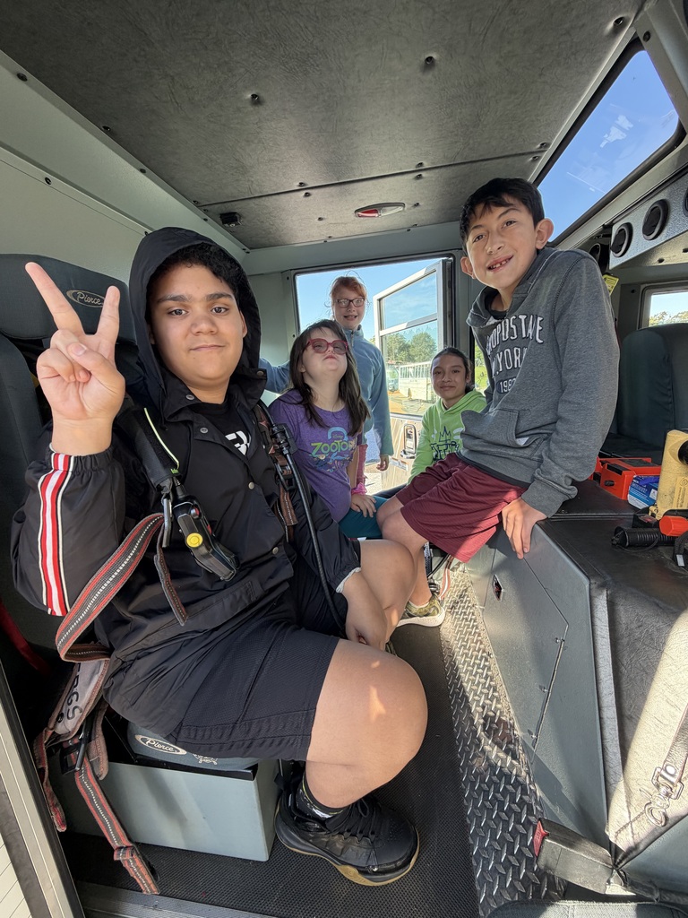 People sit inside a vehicle; two in front, two seated on a bench, and two standing near the open door.