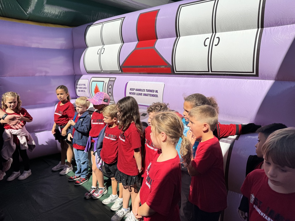Group of children in red shirts, lined up in front of a large inflatable with a chemistry lab theme.