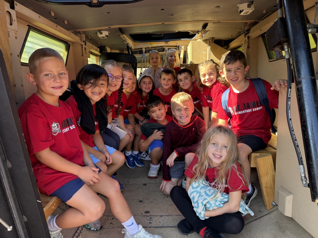 A group of children in red shirts sit inside an armored vehicle. Some hold books.