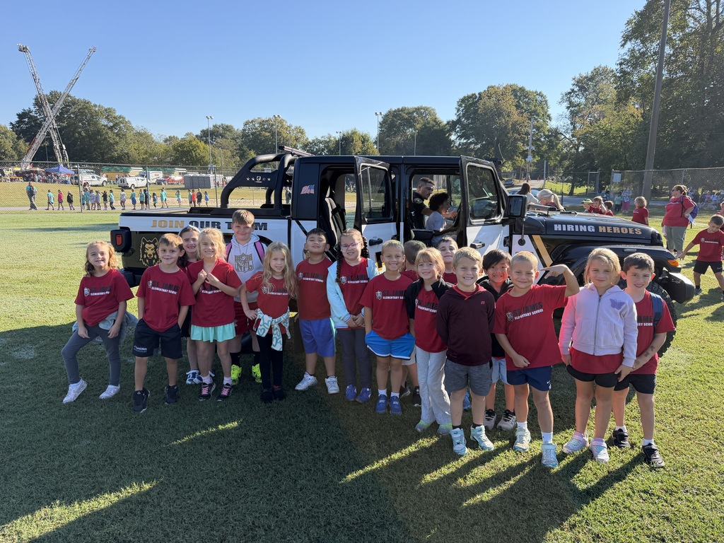 A group of young children in matching shirts pose with a large vehicle on a sunny day.