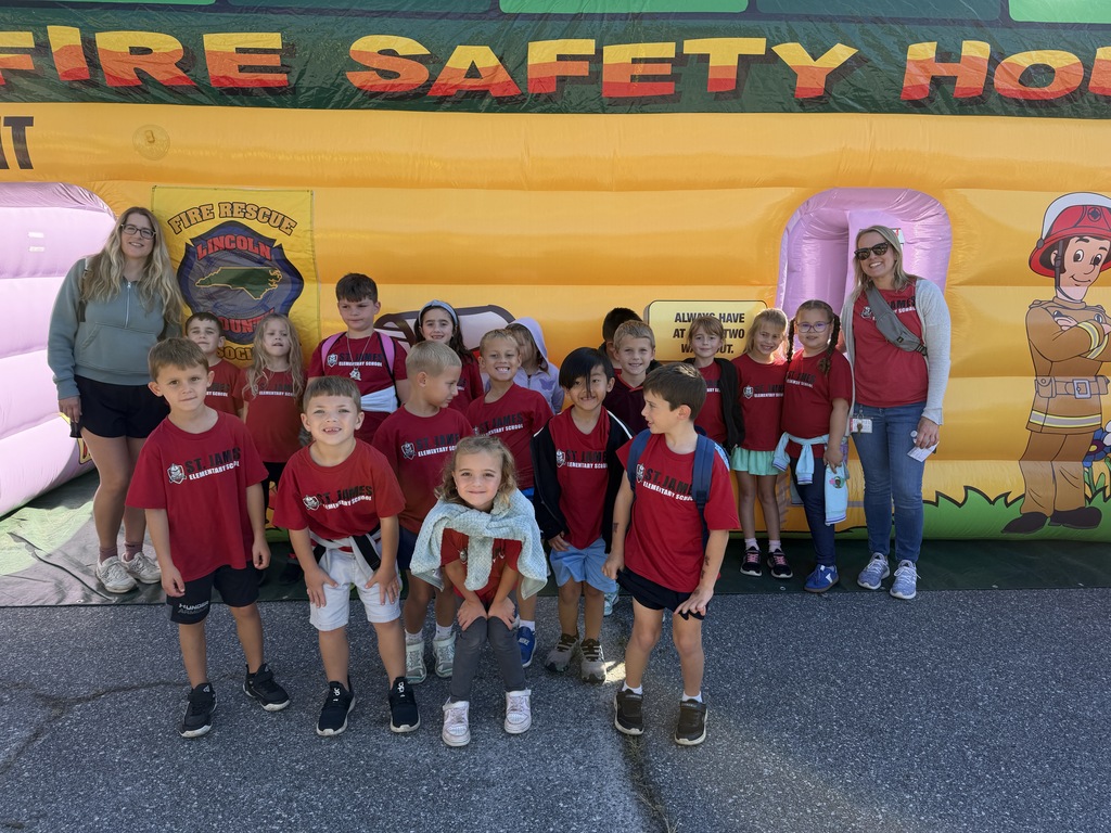 Kids in red shirts and sneakers, standing in front of a "Fire Safety Hot" inflatable playhouse with an adult.