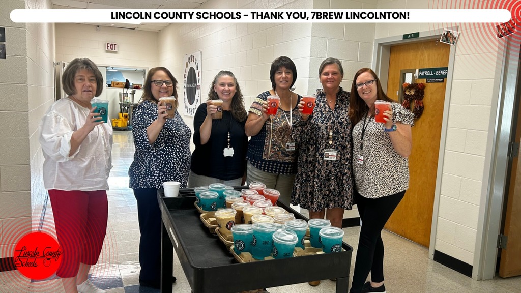 People in a hallway holding cups, likely celebrating. A table with drinks and snacks in front of them.