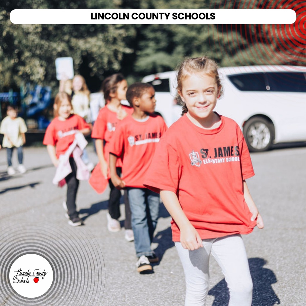 Children in red St James shirts walk in a school parking lot. A car and trees in background.