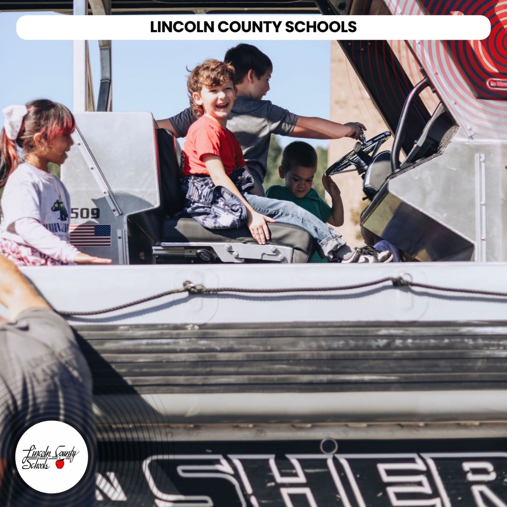 Four children ride on a police vehicle. Three sit in the driver's seat and one stands behind.