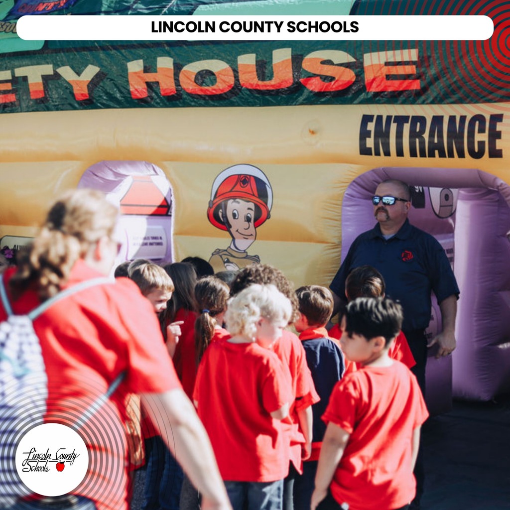 A group of children in red shirts waiting in line to enter a "Safety House" inflatable.