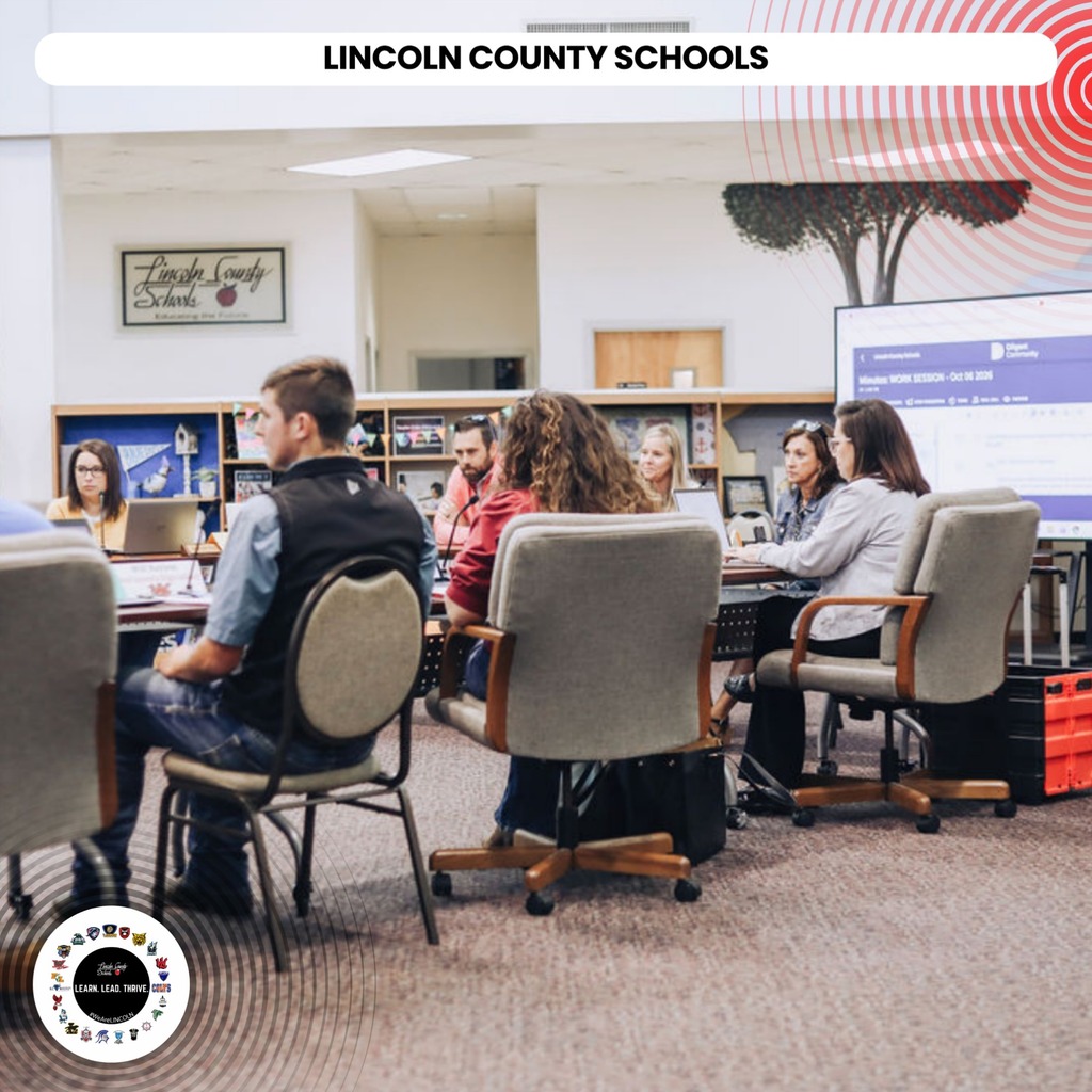 A group of people sit around tables in a room. A screen shows "LINCOLN COUNTY SCHOOLS".