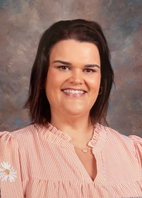 Woman with short hair wearing a pink blouse. She has a warm smile and is posing against a textured background.