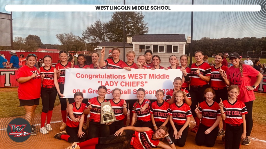 A group of girls in red uniforms holds a banner. Some crouch, some stand; one holds a trophy.