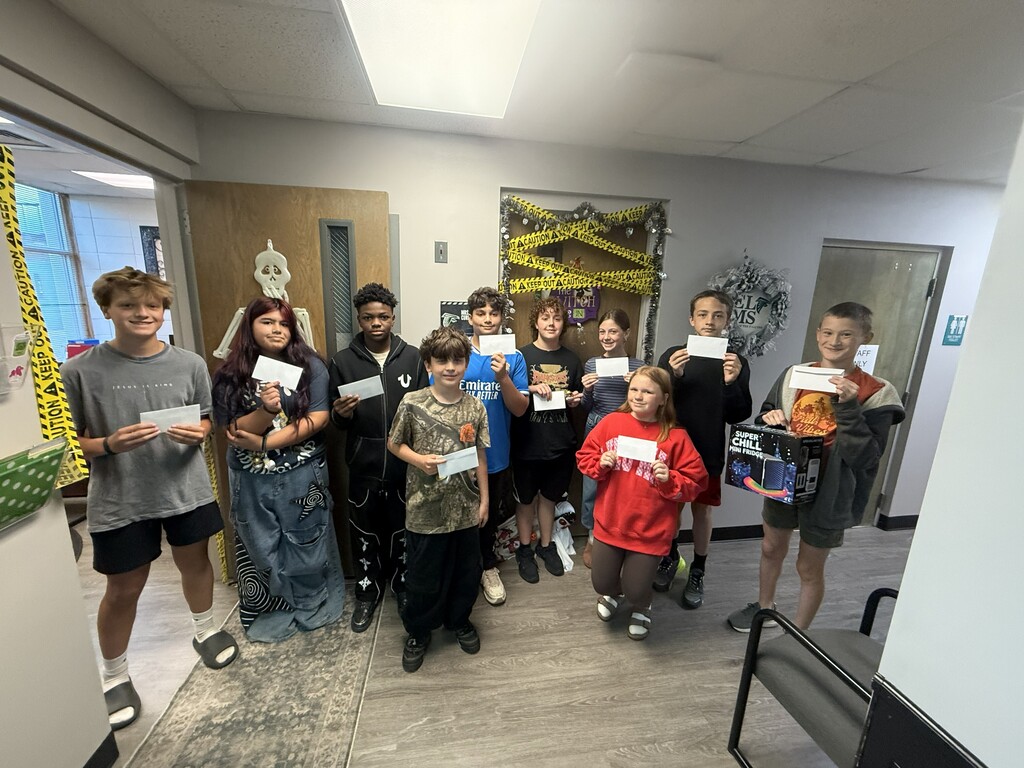 A group of students holding certificates in a corridor with white walls and a tiled floor.