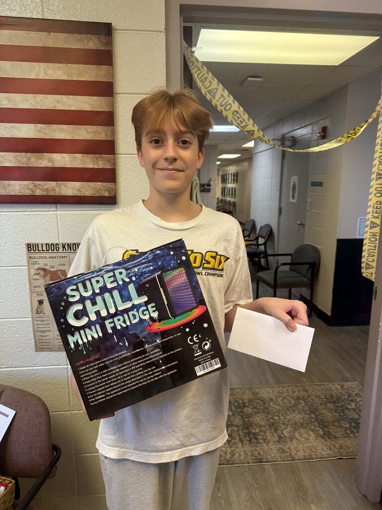 Boy holding a box of Super Chill Mini Fridge with a receipt. American flag on wall.