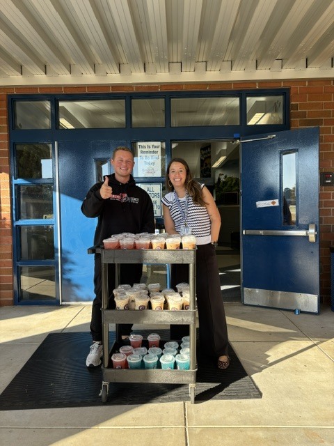 Two people stand by a cart full of cups in front of a blue door.