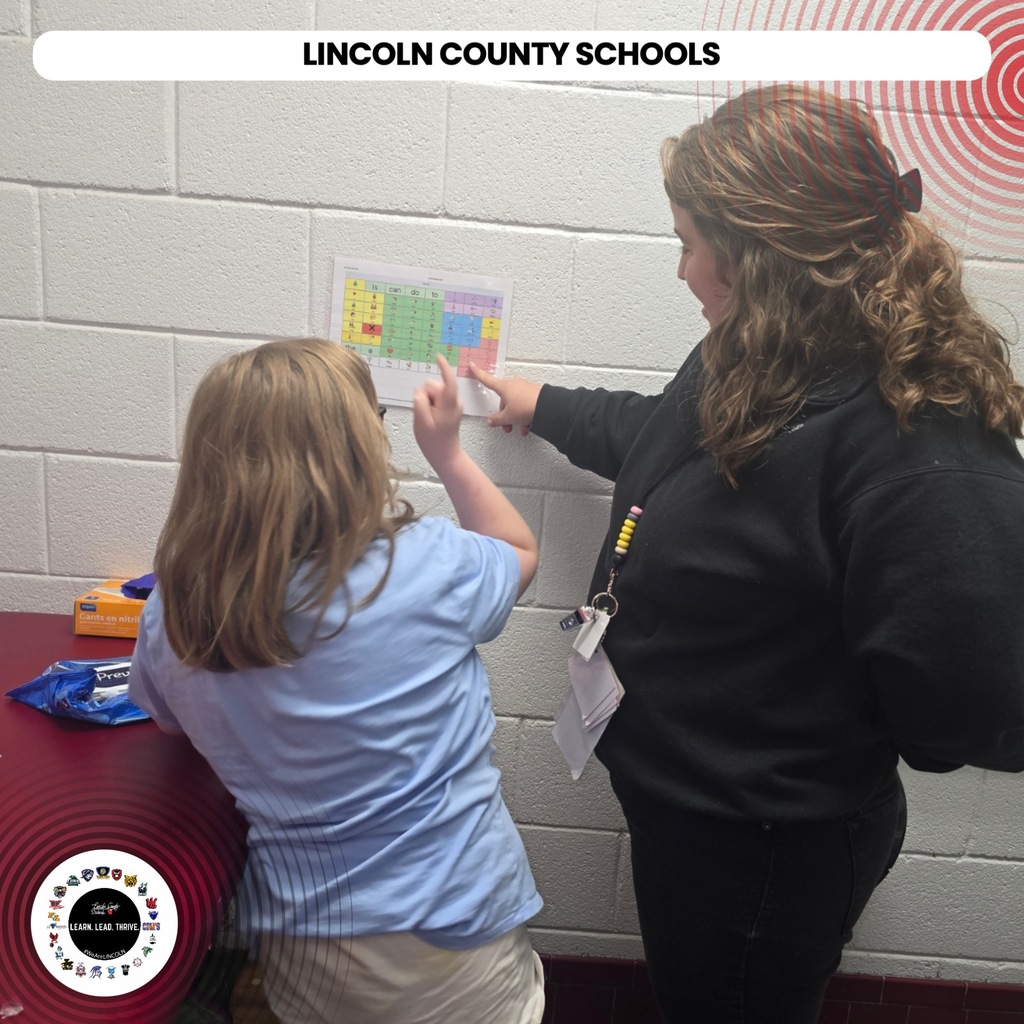 Two people inside a school room. A child points to a calendar on the wall.