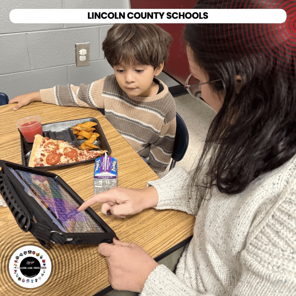 A woman and boy sit at a table. The woman holds a tablet. The boy has pizza and juice.