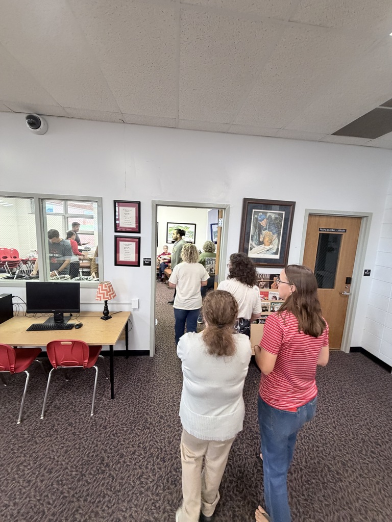 Several people stand in an office, with a woman in a white shirt facing a computer on a desk.