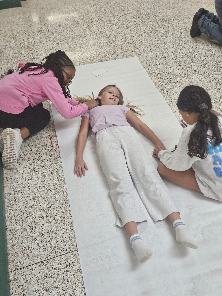 Three children, one lying on a white sheet, one kneeling, and another sitting, with tiled floor in background.