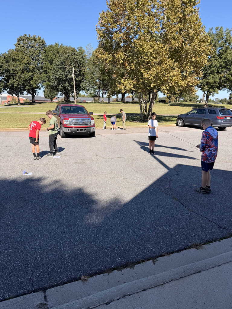 A group of children play in a parking lot, with a red pickup truck and a gray SUV parked nearby.