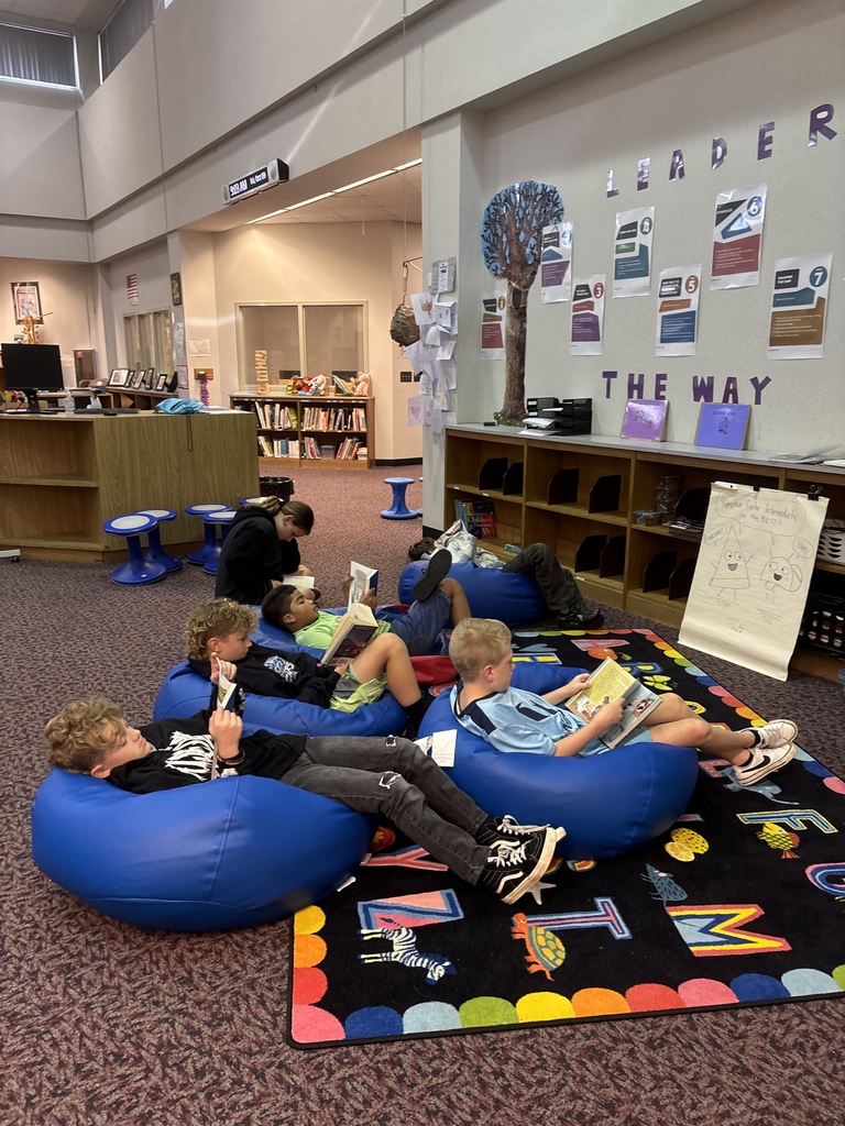 A group of children sitting on bean bags, reading books in a room with carpeted floor.