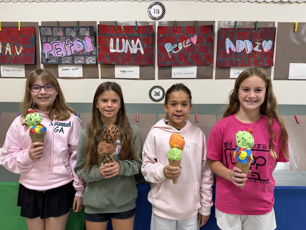 Four girls pose for a photo while holding ice cream cones. They are standing near a wall with various posters.