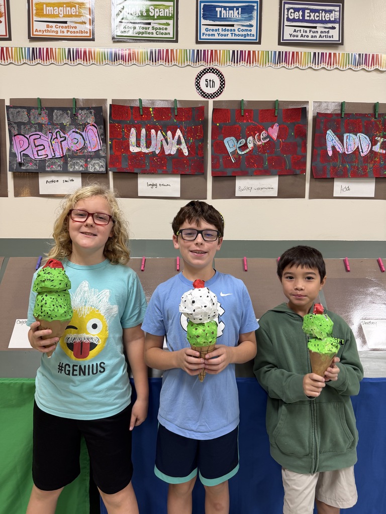Three children hold ice cream cones. Two wears glasses. Behind them, colorful signs hang on a wall.