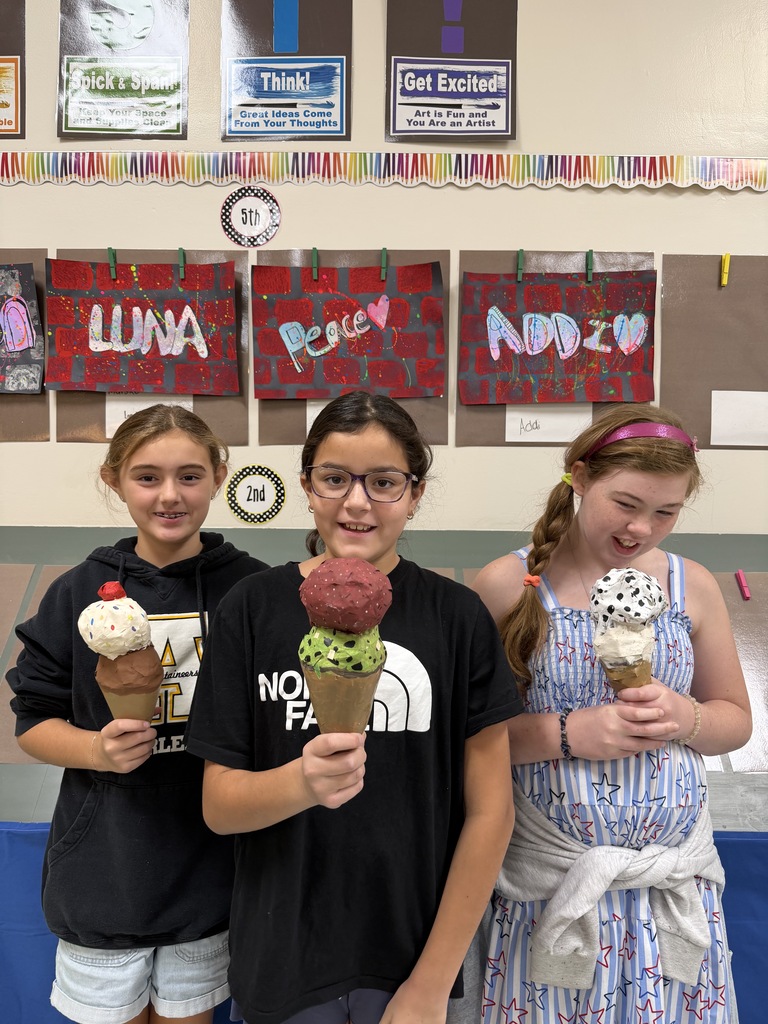 Three girls stand together holding ice cream cones. One wears glasses, another a blue dress. Behind them are colorful posters on a wall.