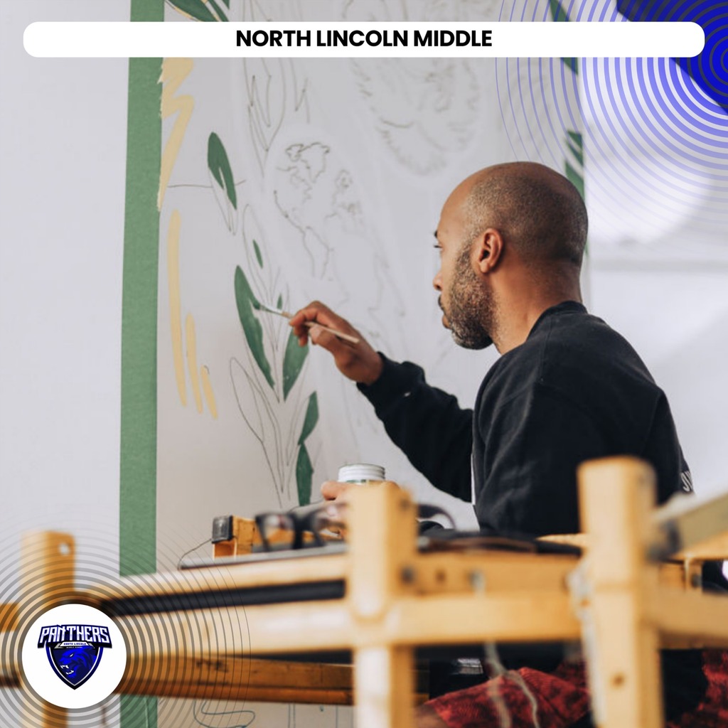 A man painting a mural with a brush, seated at a table in front of a white wall.