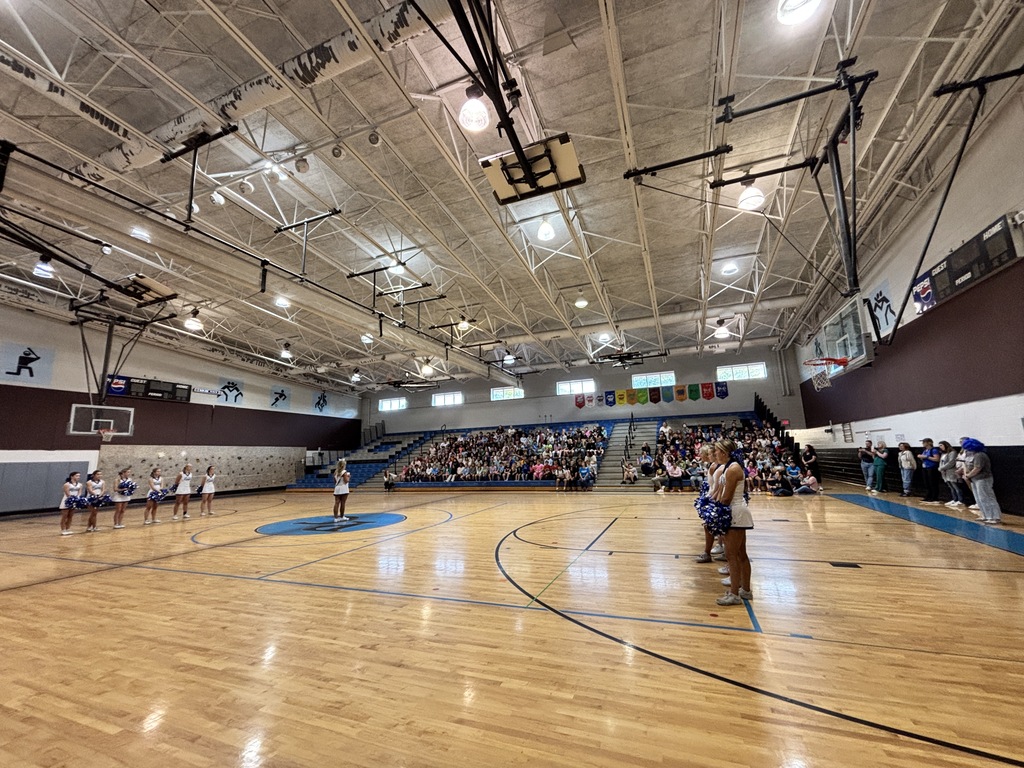 A basketball court with a large crowd of people watching a cheerleading team perform at the center.