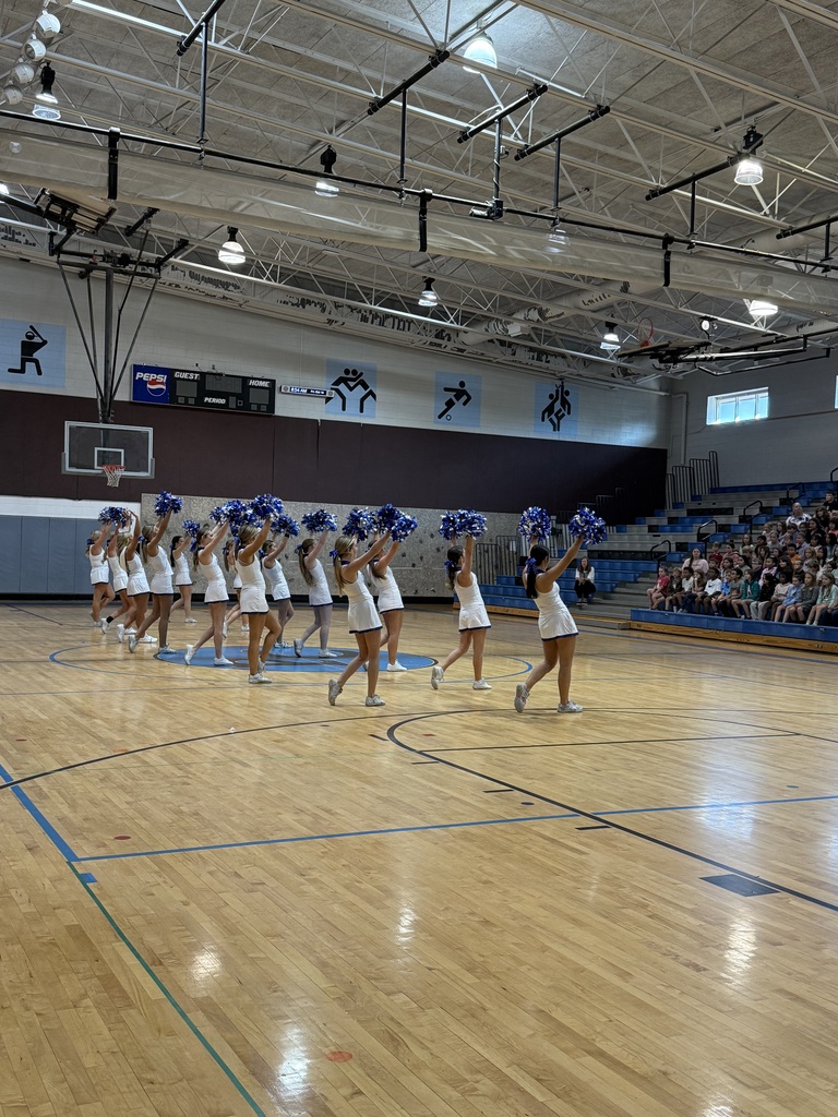A group of cheerleaders perform on a basketball court with a crowd of spectators watching.