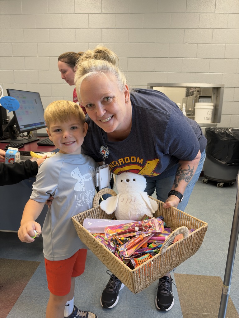 A woman and a boy stand in a room. The boy holds a basket of candies and a toy.