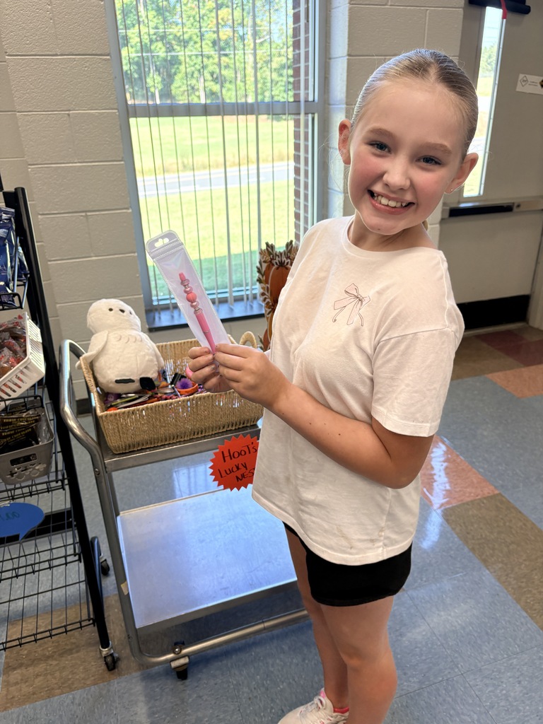 A smiling young girl holds a pink object while standing in front of a cart.