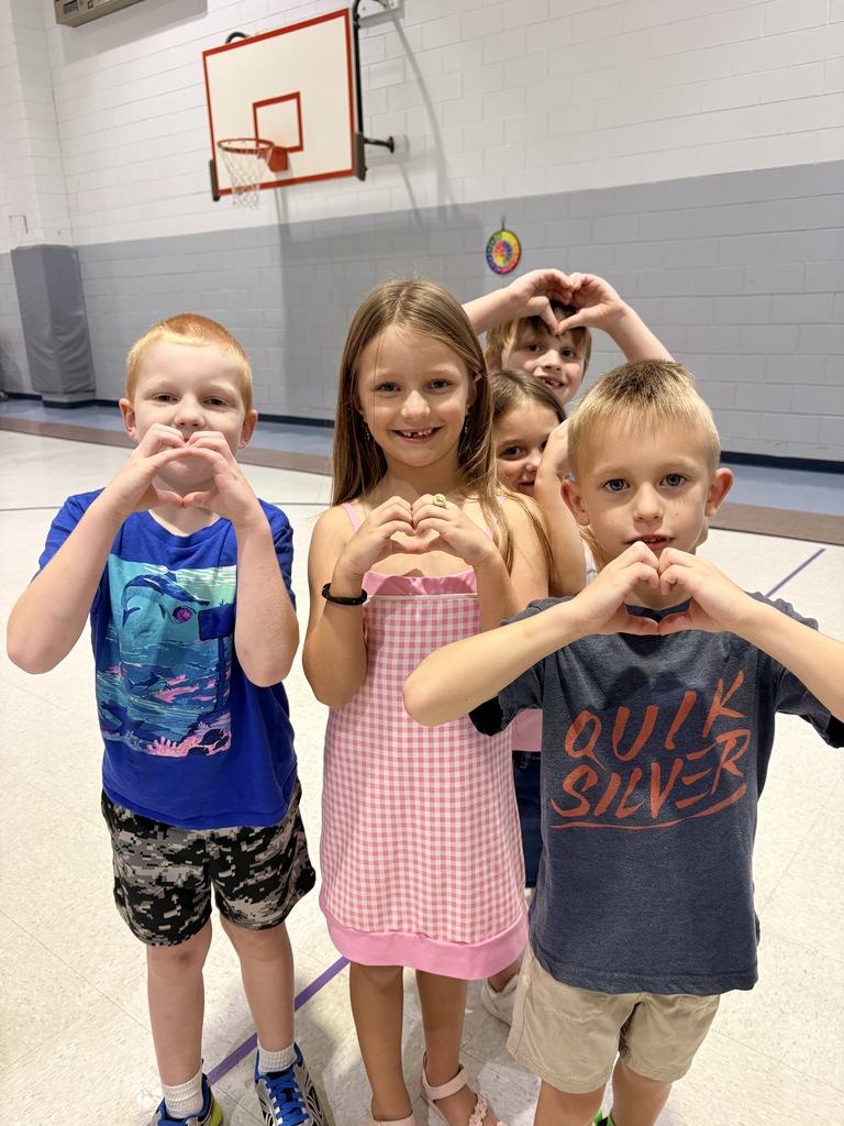 Five children, four boys and one girl, standing in a gymnasium with hands forming a heart shape.