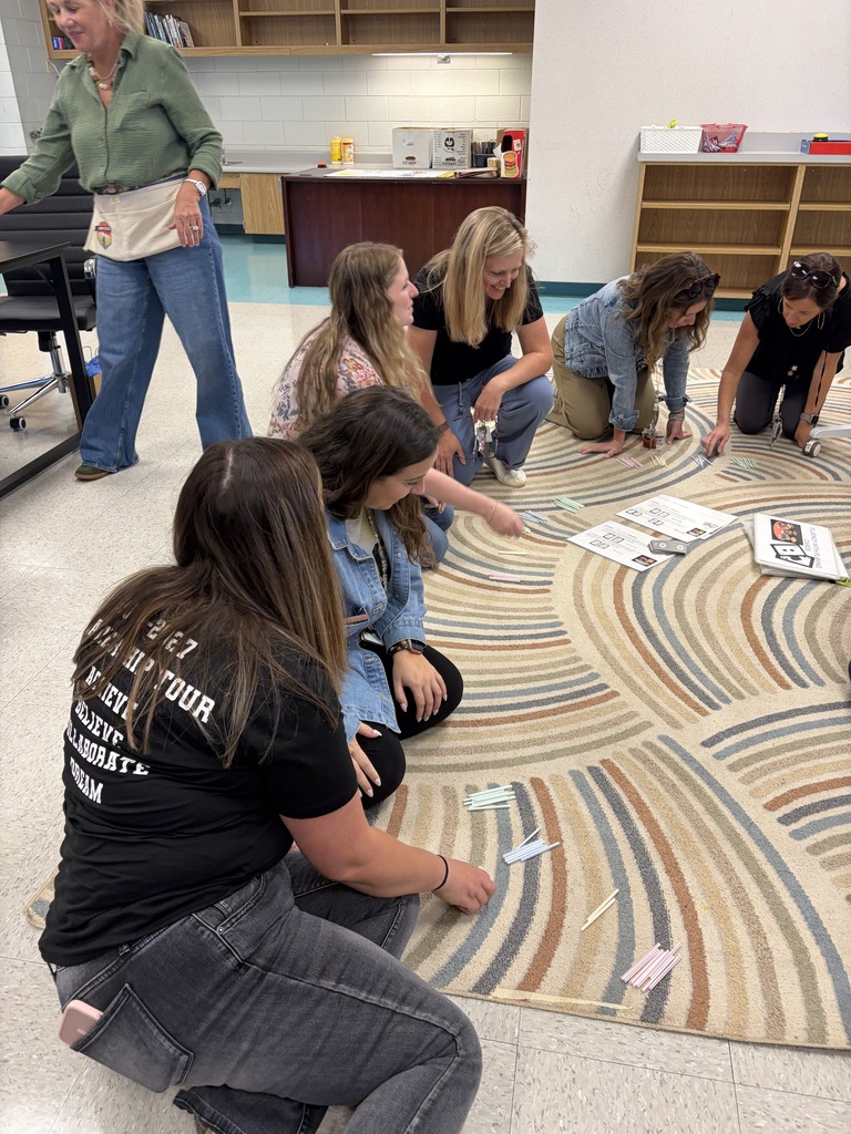 Women sitting on floor and kneeling around a rug with colorful shapes, looking at papers