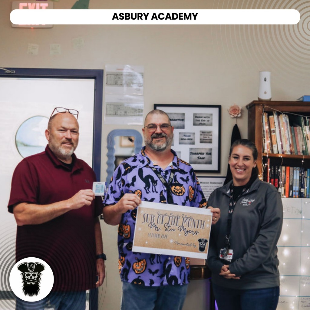 Three adults stand in a room with a bookshelf behind them. One holds a framed certificate, another a card.
