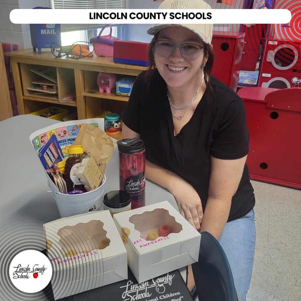 A smiling woman sits at a table with boxes of doughnuts and a box of snacks.