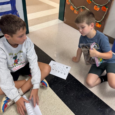 Two boys sitting on floor holding papers and items.