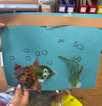 A blue piece of paper with a fish and plant on it is held by a hand.