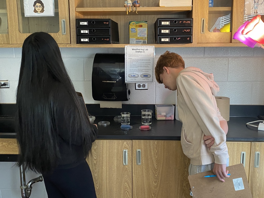 Students with long hair and a red-haired boy work together at a counter in a lab.