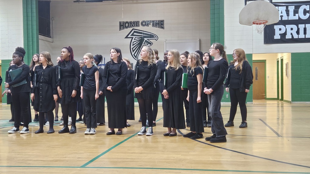 Group of students in black outfits standing on a basketball court, facing forward with a basketball hoop in the background.
