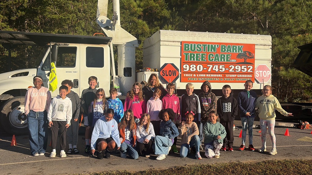Students in front of a truck with a sign that reads "BUSTIN BANK TREE CARE" and contact number.