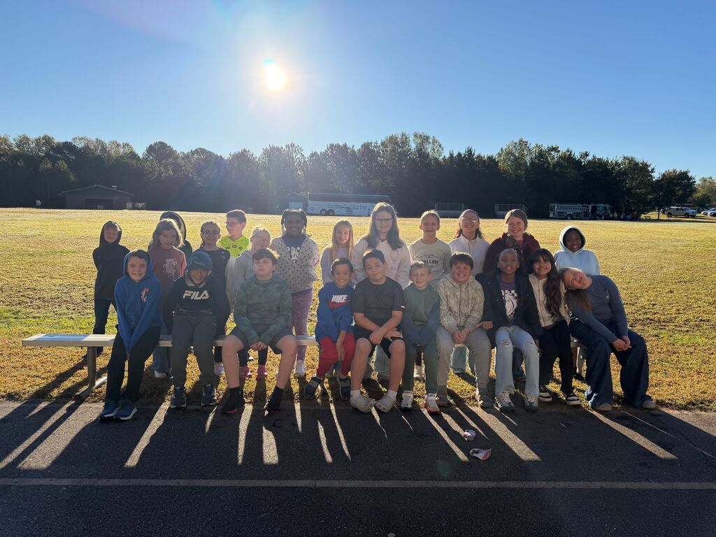 Many students pose for a group photo on a track, with a field and trees in the background.