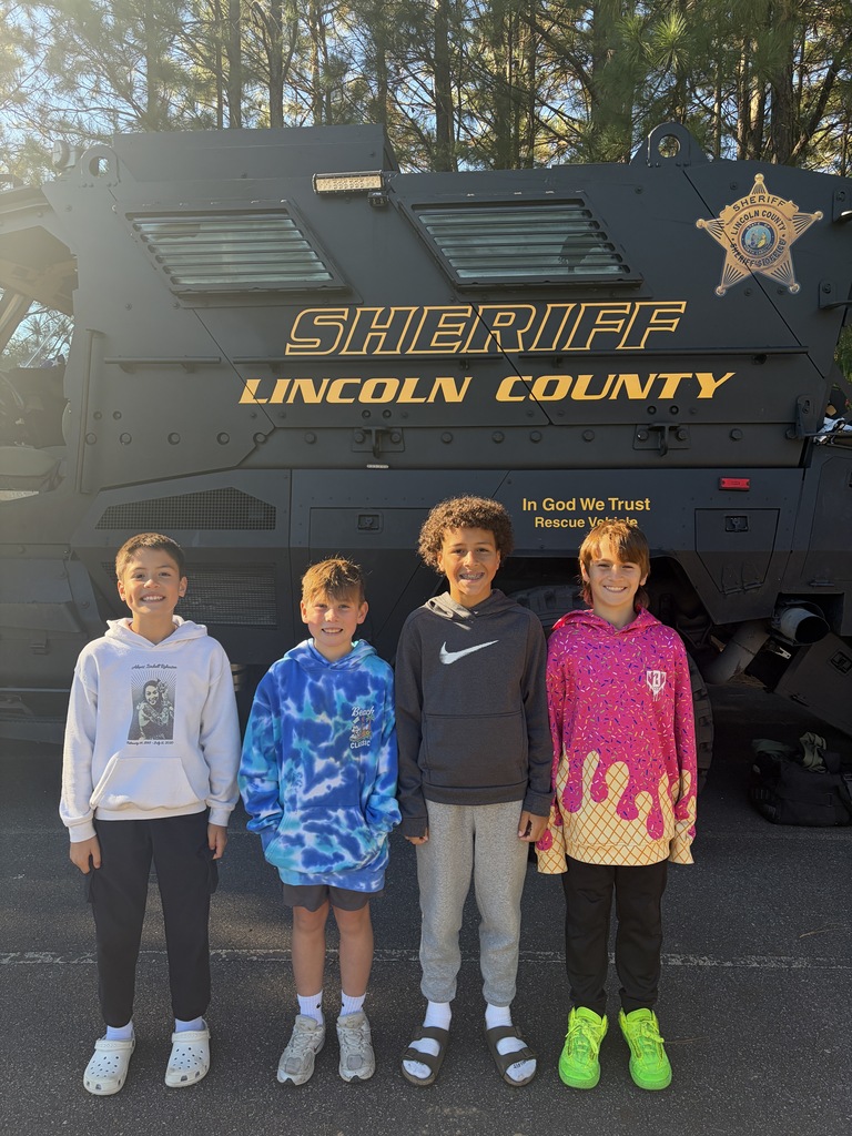 Four children stand in front of a large police vehicle with the text "SHERIFF LINCOLL COUNTY" on it.