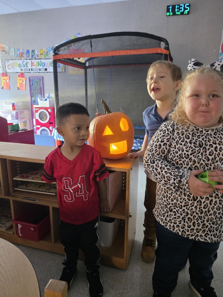 Three children in front of a shelf with a pumpkin carved as a jack-o'-lantern.