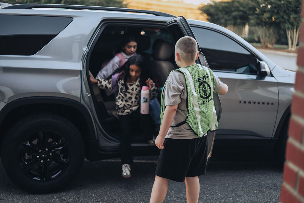Two children in an open SUV, one holding a bottle, with a person in reflective vest.