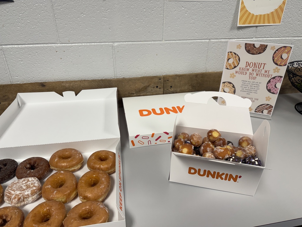 Three boxes of donuts sit on a table. Two boxes are white with the Dunkin' logo and contain a variety of donuts.