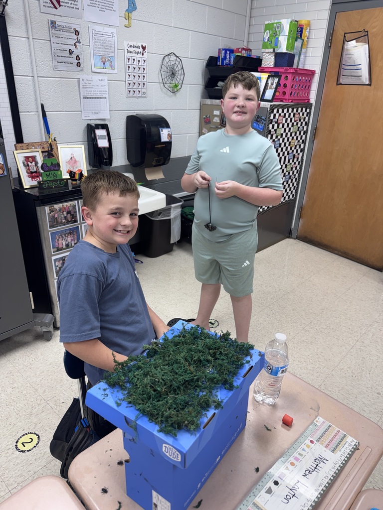 Two boys are standing in a classroom. One is holding a golf club, the other is smiling.