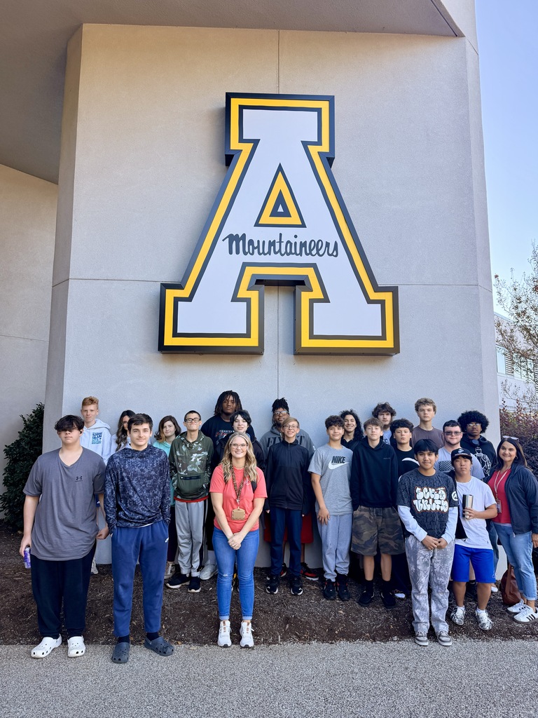 Students stand in two rows in front of a building with a yellow ASU logo above.